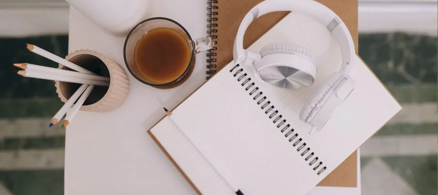 Headphones sitting on top of a notebook with a cup of coffee next to them.
