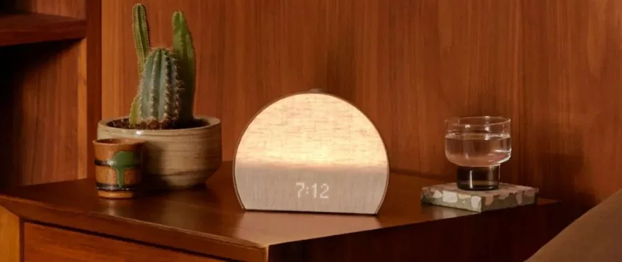 Hatch alarm clock sitting on a nightstand next to a glass of water.