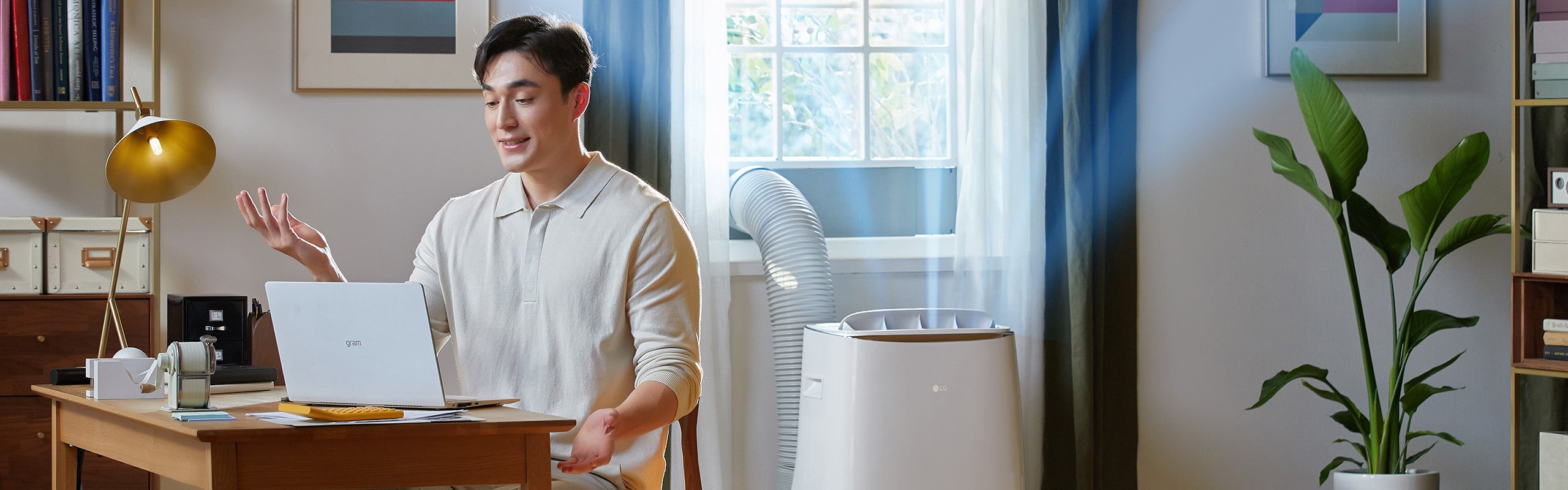 A man sitting on a video call on his laptop while an air conditioner behind him pumps cold air into the environment