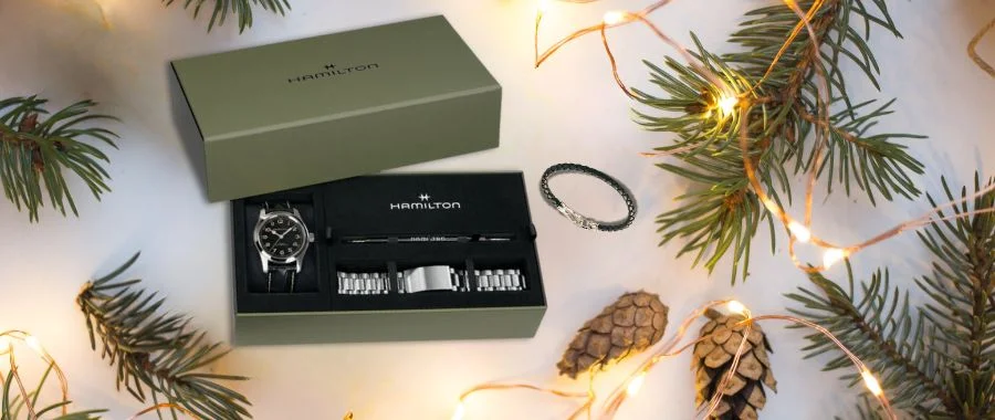 A Hamilton watch set in a green box surrounded by holiday evergreen boughs and twinkle lights