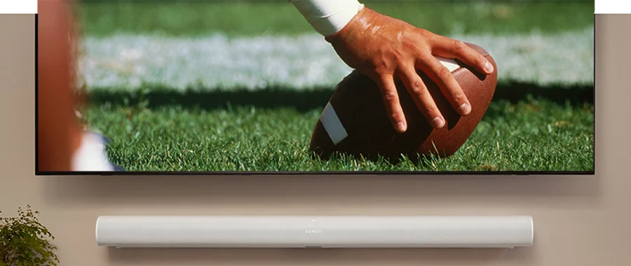 A white soundbar mounted on the wall underneath a TV displaying a football game