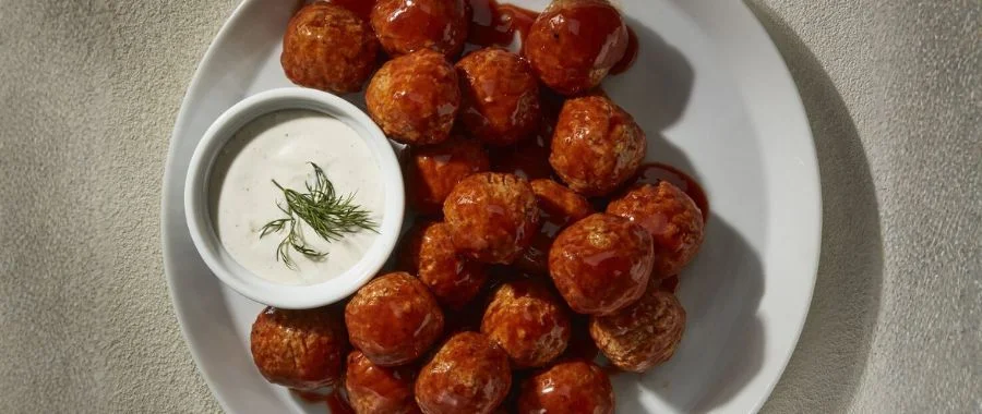 Plate of buffalo chicken meatballs and a side of ranch garnished with a sprig of dill.