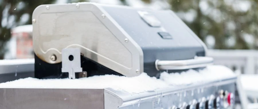 A propane grill on a porch, slightly covered with snow.