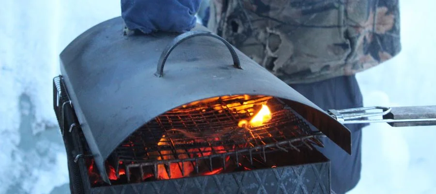 A man using a charcoal grill in the winter.