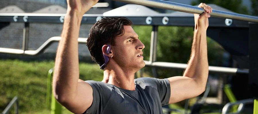 A man wearing the Endurance Pace headphones by JBL as he does outdoor pull-ups