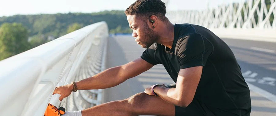 A man stretching his legs on a bridge while wearing the new JBL Endurance Zone earbuds
