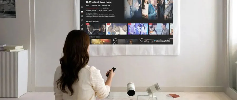 Woman sitting on a sofa with the Samsung Freestyle+ projecting Netflix onto the wall in front of her.
