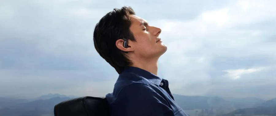 A man wearing the Shokz OpenFit Pro earbuds while sitting next to a window.