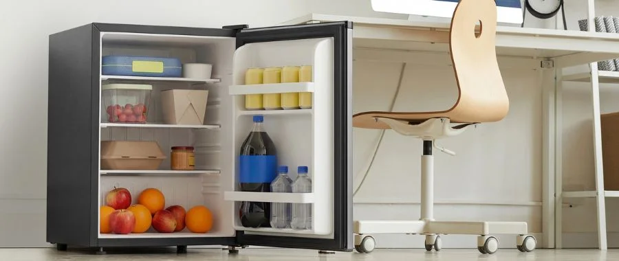 An open mini fridge beside a desk and desk chair.