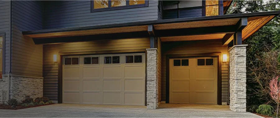 Beige, custom garage doors on a modern house with the outside lights on.
