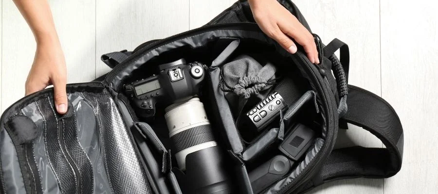 Overhead view of person closing a camera bag with DSLR camera, smaller camera, lenses and other accessories.