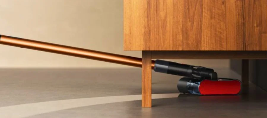 The Dyson PencilWash vacuum cleaning under a piece of furniture.
