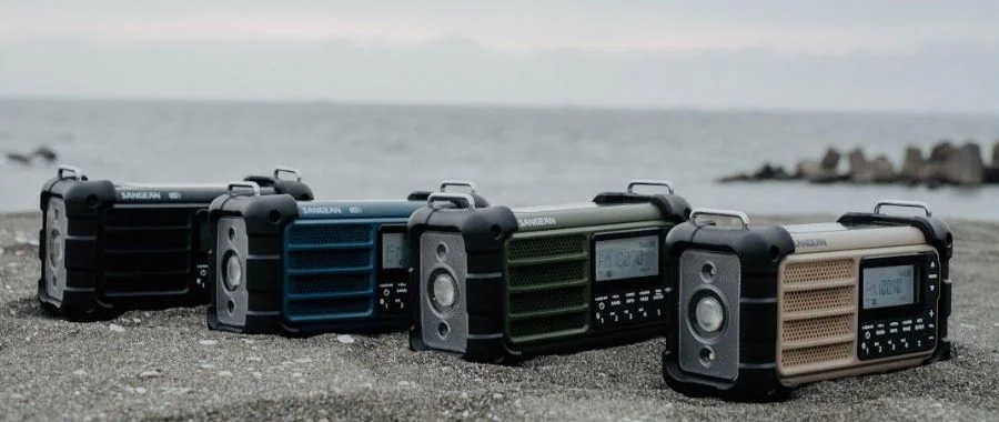 Four Sangean radios lined up in front of choppy waters