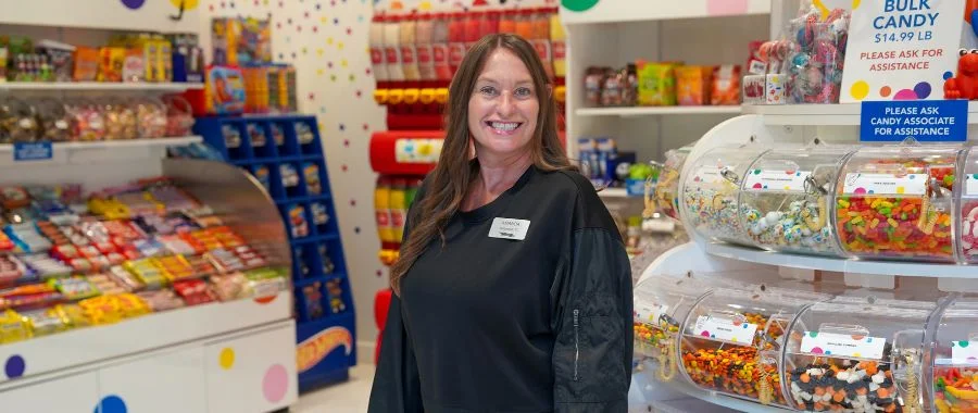Amanda Dukala smiling in the Candy Store beside the bins of bulk candy.