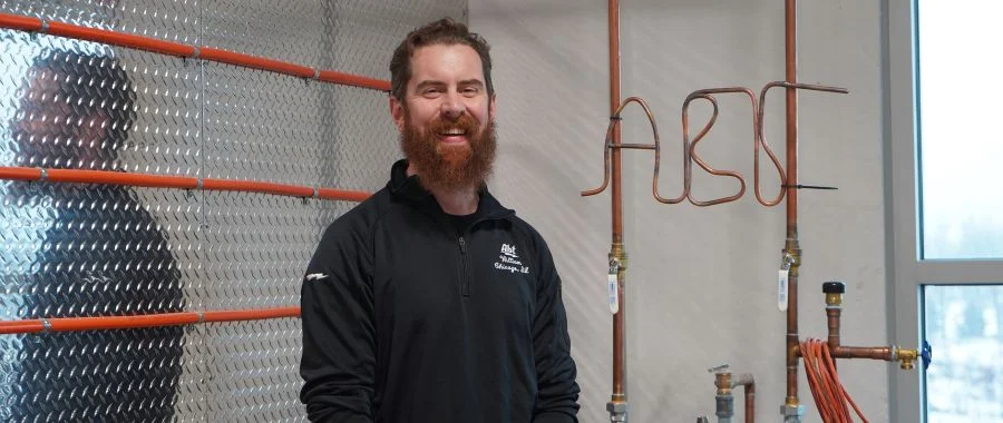 Bill O'Callaghan smiling beside copper piping and wiring that spells out 'ABT'