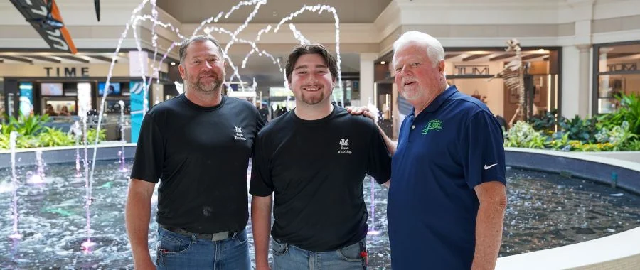 Jason, Devon and Terry Forrest smile in Abt's Atrium in front of the fountain