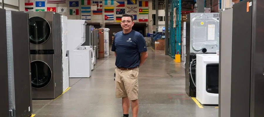 Jose Perez in the Abt warehouse. Beside him are appliances like stackable washers