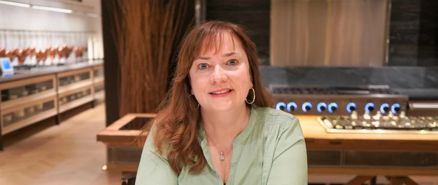 Margaret Herzog sits in the Inspiration Kitchen at Abt in green, smiling.