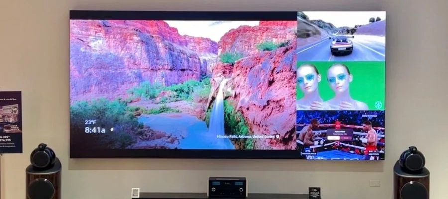 A Just Video Walls television display at Abt displaying three small screens and one large one, all as one television. The smaller screens showcase a boxing match, a woman in green and a driving video game.
