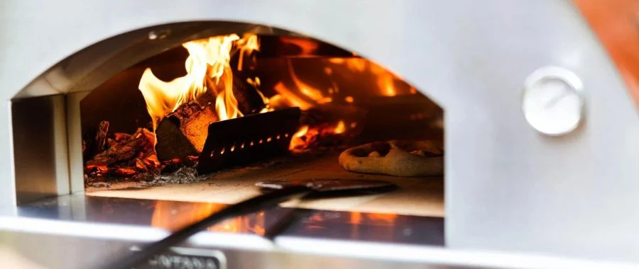 Person using a pizza peel to remove a pizza from Fontana wood-fired pizza oven.