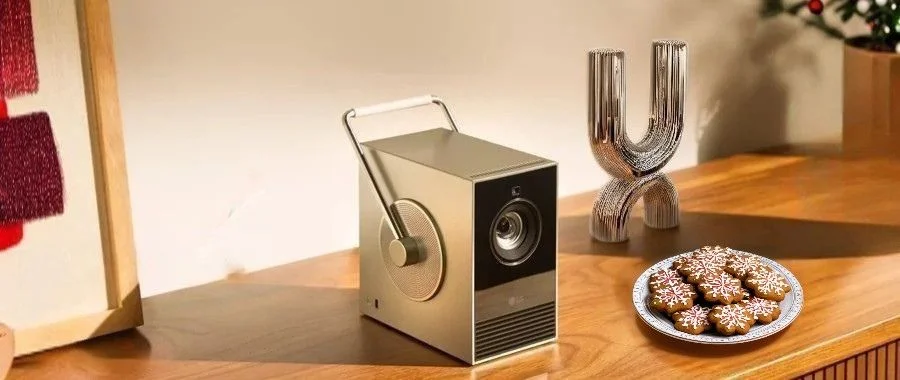 The LG CineBeam Q projector sitting on a wooden table next to a plate of gingerbread cookies.