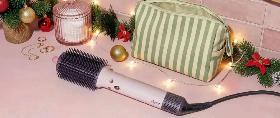 Dyson Airsmooth hot brush on a bathroom counter next to a green striped makeup bag.