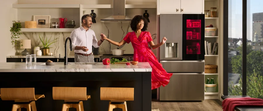 A couple dancing in the kitchen wearing holiday colors. A door-in-door refrigerator is behind them