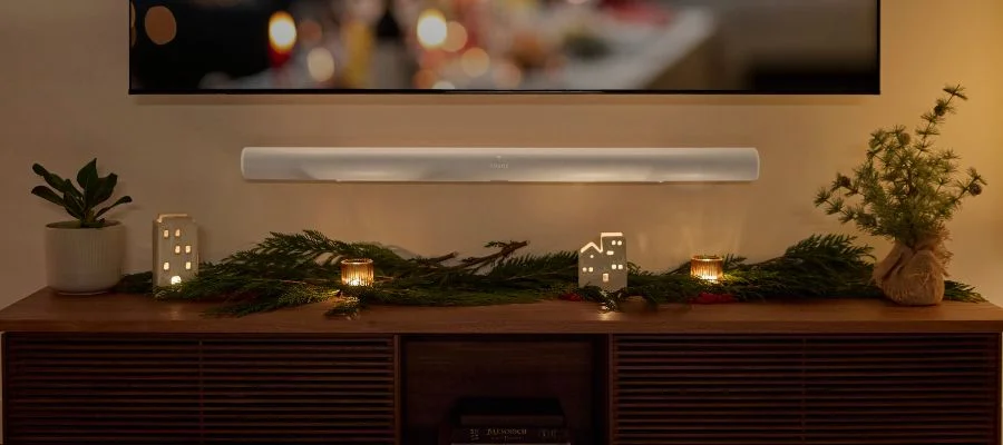 A Sonos Arc soundbar below a TV and above an entertainment center decorated with seasonal greens and candles