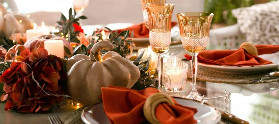 A table decorated with seasonal tableware, glassware, florals and a faux pumpkin.
