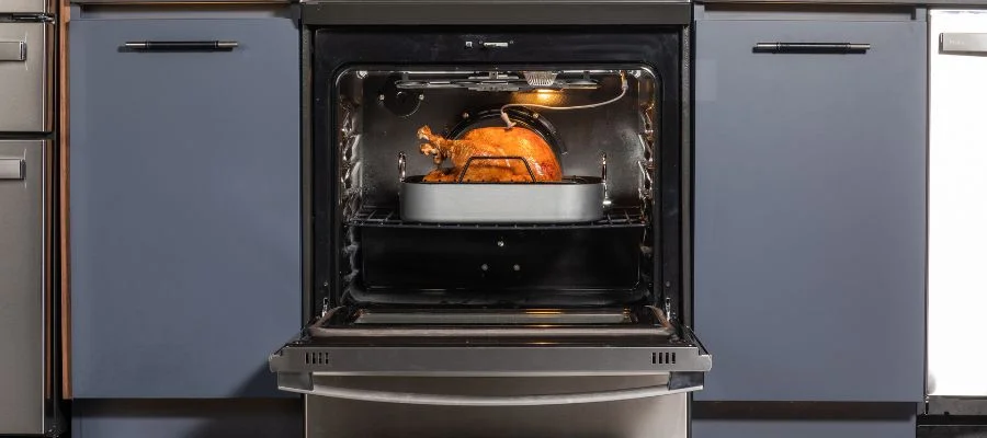 A turkey cooking in an open oven. Blue-gray cabinets are on either side