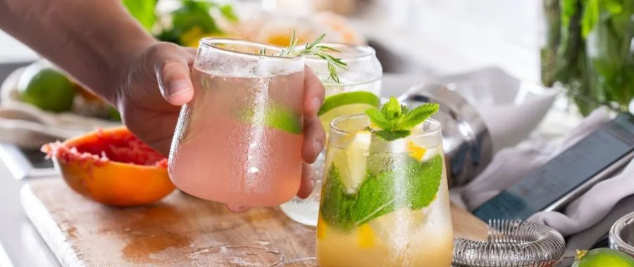 A hand holding a pink cocktail in a stemless glass