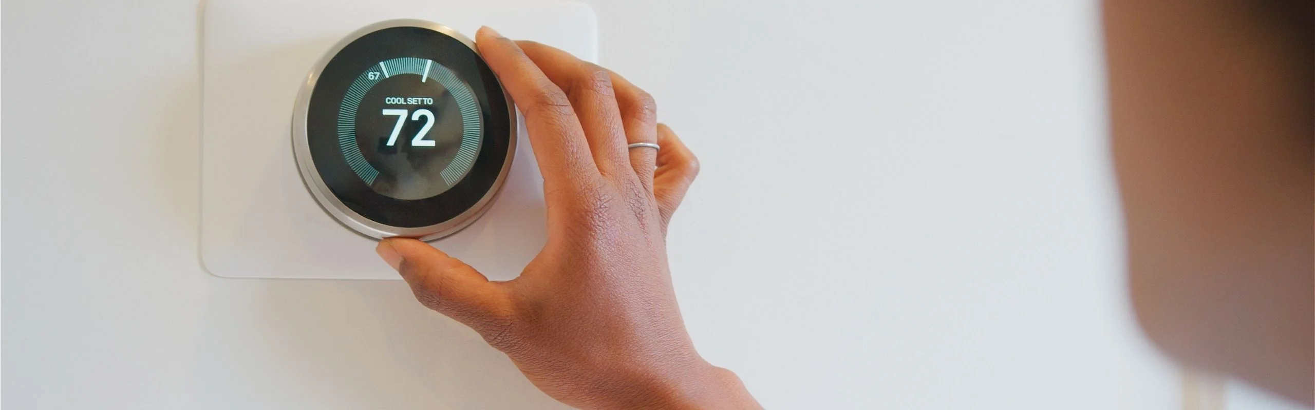 A person adjusting a smart thermostat with a digital screen, setting the AC to 72 F manually.