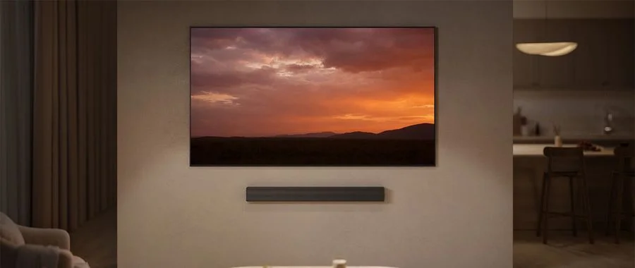 Samsung HW-QS90H soundbar mounted underneath TV with a sunset on screen