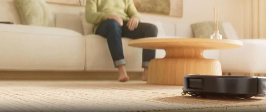 An iRobot Roomba robot vacuum cleaning a rug in a modern living room.