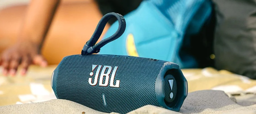 A blue JBL Charge 6 resting in the sand on a beach