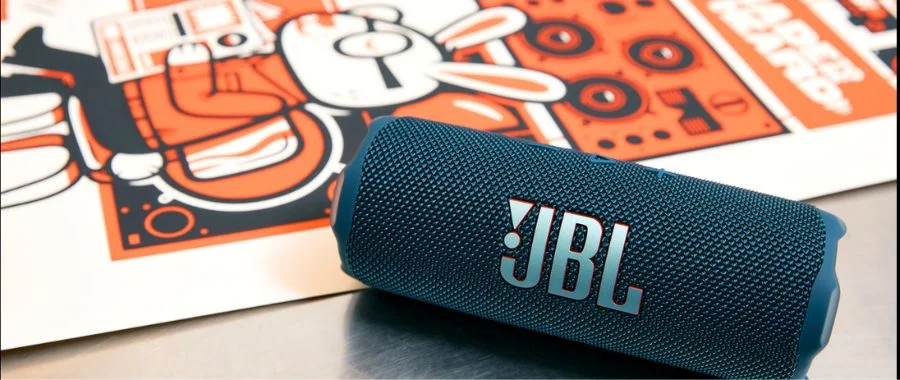 A blue JBL Flip 7 speaker beside a fresh print on a table in an art studio
