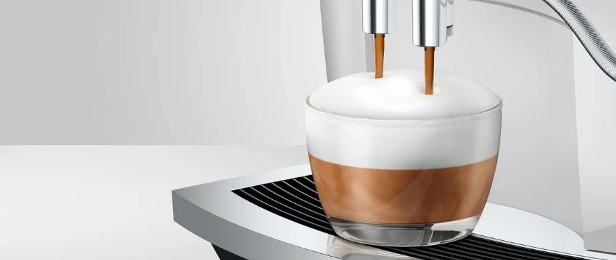 Closeup of platinum Jura E6 espresso machine brewing a cappuccino in a glass cup.