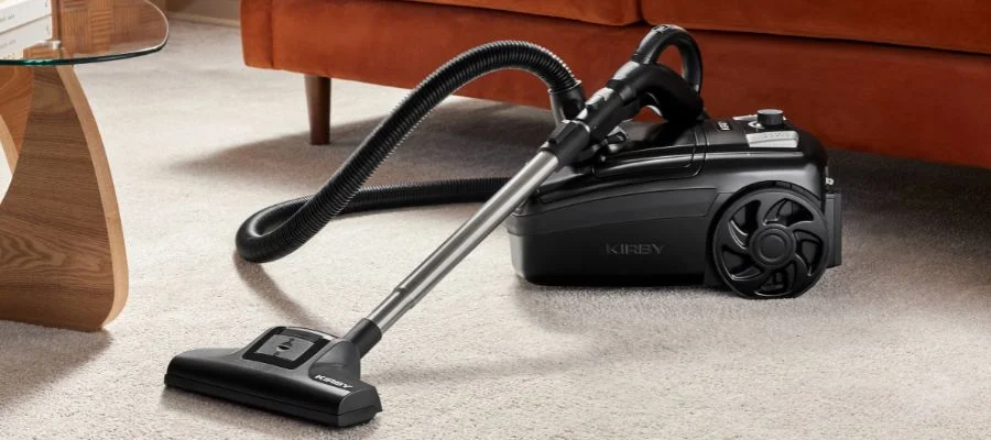 The Kirby C530 canister vacuum is on the carpet beside an orange couch in a living room.