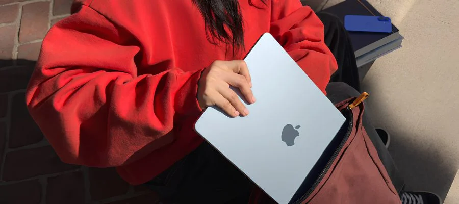 Person in a red sweatshirt sliding a MacBook Air into a backpack.