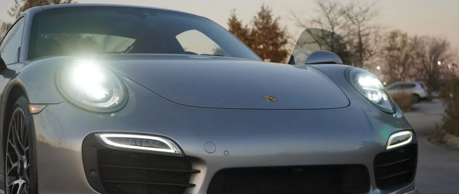 Silver porsche at sunset with its headlights on