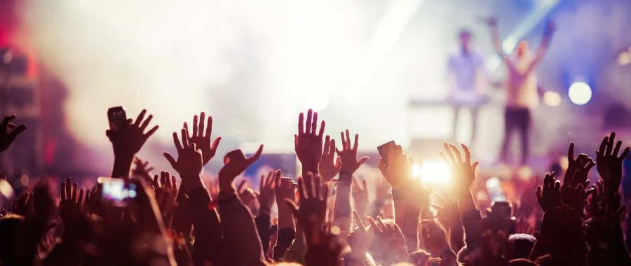 Festival crowd with their hands up, with a band performing in the background.