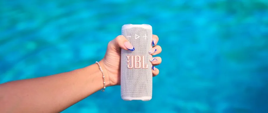 Person with blue nail art holding white JBL Grip speaker over a pool