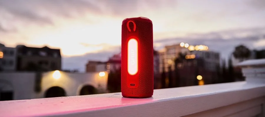 Red JBL Grip speaker sitting on the ledge of a building. City buildings are in the background.