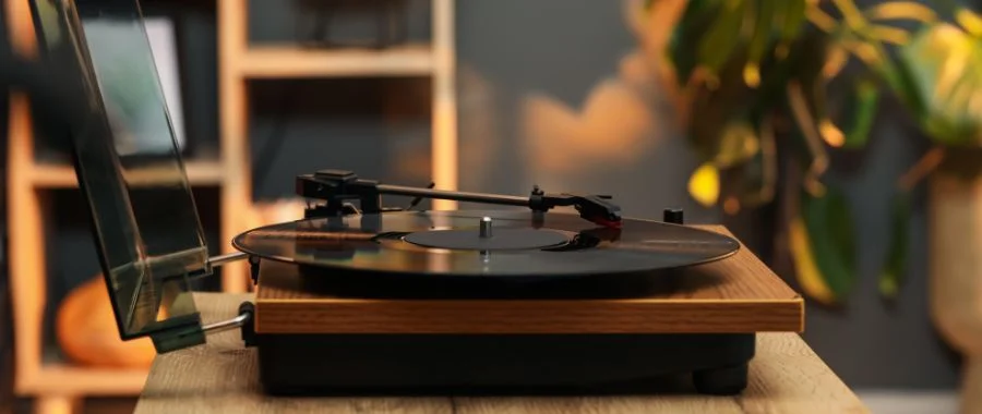 A modern turntable sitting on a small wooden table with plants in the background.