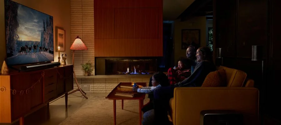 A family in the dark lounging on the couch and watching TV/listening to their soundbar