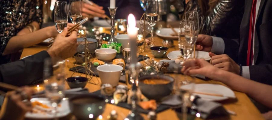 A dining table set up with champagne flutes, candles, plates, bowls and people dressed formally