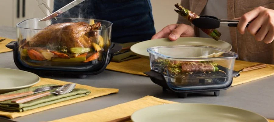 Poultry and veggies about to be sliced into in one glass container. In the other, bacon-wrapped asparagus are served.