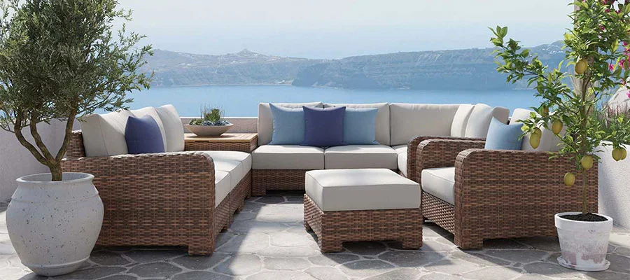 wicker sectional and ottoman with beige cushions and blue pillows with a view of a lake in the background