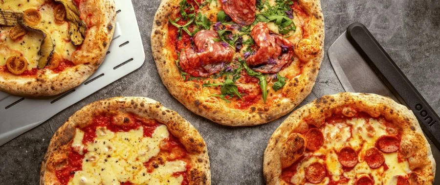 Four wood-fired pizzas sit on a counter alongside an Ooni pizza cutter.