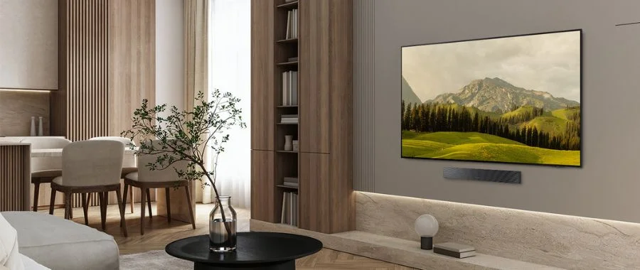 Samsung S85F TV mounted on a wall above a soundbar in front of a beige sofa.